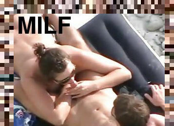 Brown-haired milf sucks and rubs her BF's shaft on a nude beach