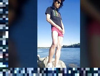 Twink boy with long dark hair pissing pee on the river dressed in glasses cap sneakers boxer tshirt