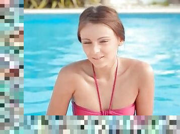 Petite pretty girl in pink bikini emerges from the pool