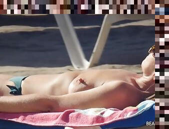 Topless leggy milf reads magazines at the beach